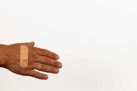 A hand with a simple bandage on the palm rests against a neutral background, highlighting the injury and effort to heal. The skin tone is visible in detail.の写真素材