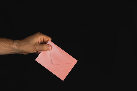 A hand extends to present a pink envelope in a dark setting, suggesting anticipation or an important message, capturing a moment of connection.の写真素材