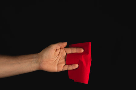 A hand extends outward, showcasing a folded red piece of material against a black backdrop, creating a striking contrast and inviting intrigue.の写真素材