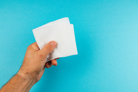 A hand grips a few white napkins, ready for use. The vibrant blue background emphasizes the simplicity and utility of the napkins in any social setting.の写真素材