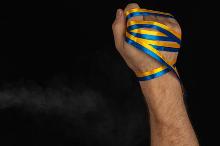 A hand clenched into a fist displays blue and yellow ribbons, symbolizing resilience and solidarity. The dark background highlights the powerful gesture.の写真素材