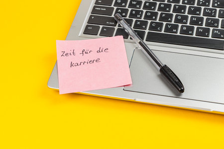 A pink sticky note on a silver laptop keyboard reads a motivational message about career timing, with a black pen placed nearby on a bright yellow background.の写真素材