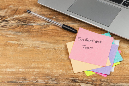Colorful sticky notes with team reminders sit beside a laptop on a wooden desk, highlighting a...