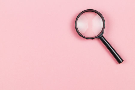 A magnifying glass rests on a soft pink surface. This simple arrangement highlights the importance of observation and clarity in any task or exploration.の写真素材