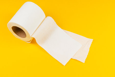 A roll of plain paper is unrolled slightly against a bright yellow background. This scene suggests use in cleaning or personal hygiene activities at home.の写真素材