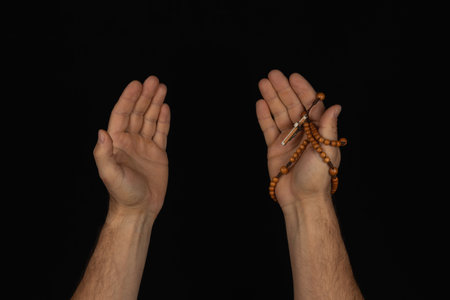 Two hands are raised, open, and relaxed, holding a string of prayer beads. The background is dark, creating a peaceful atmosphere for meditation or prayer.の写真素材