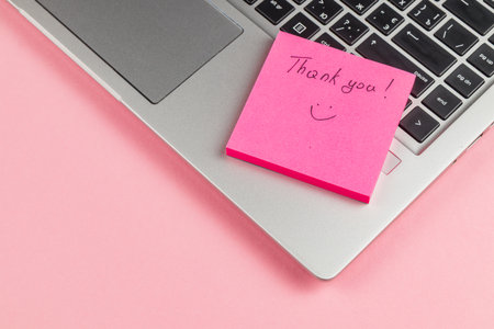 A pink sticky note with a cheerful message sits on a laptop keyboard against a light pink backdrop. It adds a personal touch to the workspace.の写真素材