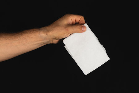 A hand grasps a stack of clean white paper towels, set against a solid black backdrop. The scene highlights the simplicity and utility of everyday items.の写真素材