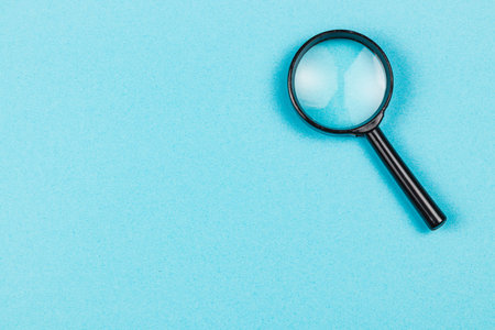 A magnifying glass rests on a smooth blue surface, inviting curiosity and investigation into the details of objects beneath it.の写真素材
