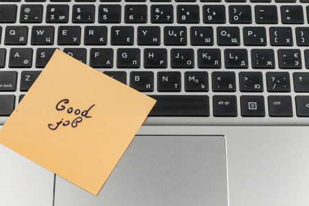A sticky note that reads good job rests on a laptop keyboard. The scene captures a moment of encouragement during a productive work session at home or office.の写真素材