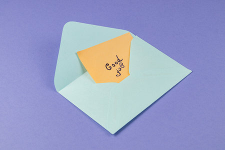 A light blue envelope is partially open, revealing a bright orange note inside that says good job. The background is solid purple, creating a cheerful atmosphere.の写真素材
