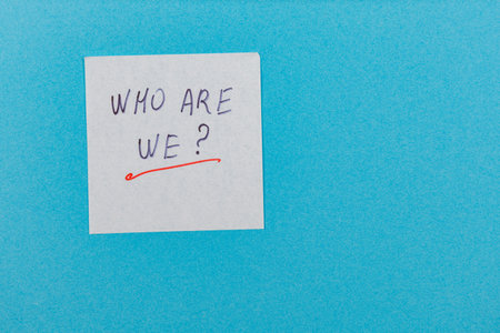 A sticky note on a bright blue background poses the question Who are we? inviting reflection on identity and self-discovery in a simple yet engaging manner.の写真素材