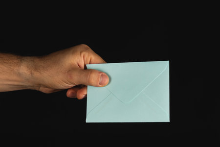 A person's hand offers a light blue envelope, showcasing a simple but elegant design. The dark background adds contrast, emphasizing the envelope's color.の写真素材