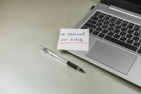 A motivational sticky note with the words Ihr SchlÃ¼ssel zum Erfolg sits next to a laptop on a clean desk. The scene conveys a workspace focused on success.の写真素材