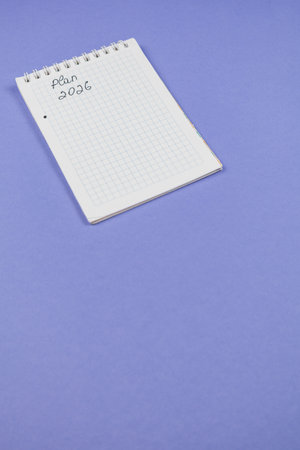 A blank notepad lies on a purple surface with the words Plan 2026 written on the first page. Ideal...