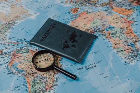 A passport and magnifying glass sit on an unfolded world map, highlighting destinations like Brazil. Perfect for planning future travel adventures and exploration.のeditorial素材