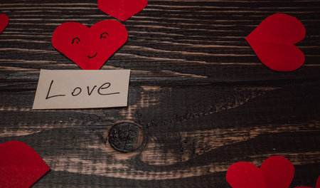 Red paper hearts are scattered around a note that has the word love written on it. This scene rests...