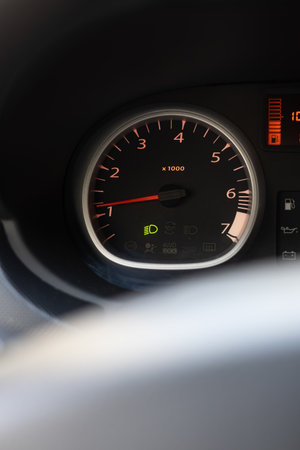 A dashboard gauge shows RPM and warning light in a car. The vehicle is likely in operation and...
