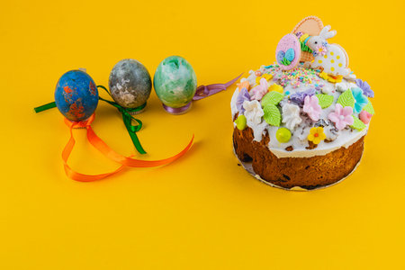 A round cake sits on a table with colorful decorations. Next to it are three Easter eggs with...