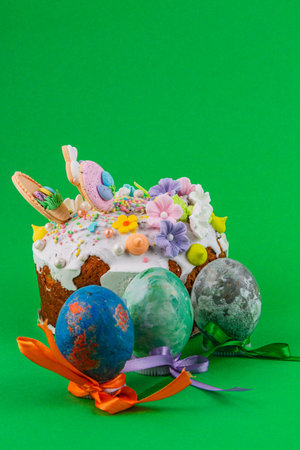 A cake is decorated with flowers and candy on top, with painted eggs placed in front. The background...