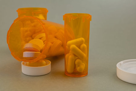 Several orange pill bottles are placed on a table. Some bottles are open and capsules are scattered...