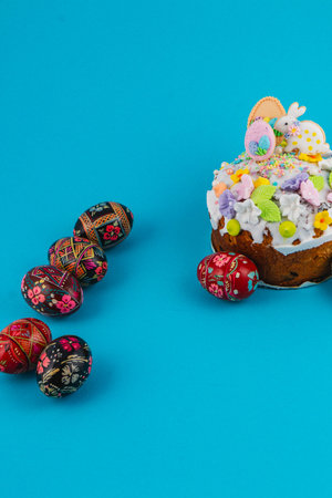 A decorated cake sits on a blue background with colorful eggs arranged beside it. The cake features...