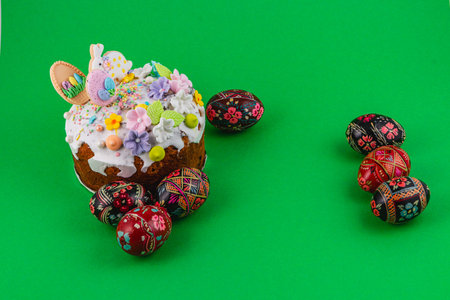 A cake with flowers and decorations sits on a green surface. Colorful eggs are arranged around it,...