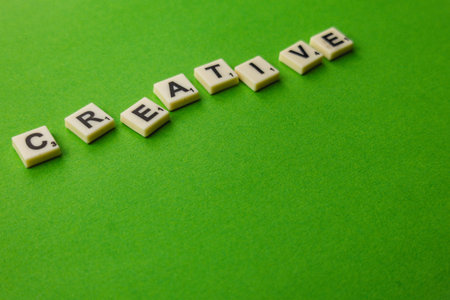 Tiles are arranged on a green surface to spell the word creative. People enjoy playing word games.
