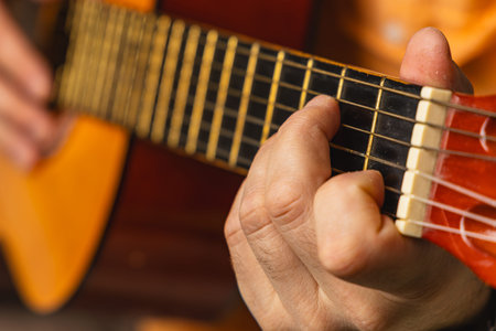 A person plays an acoustic guitar while seated, focusing on the strings and frets. Soft lighting...