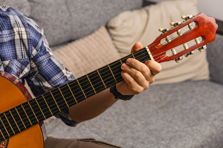 A person sits on a sofa in a living room playing guitar. The casual setting includes cushions and...