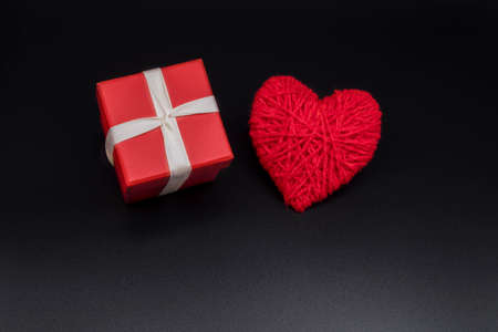 Red box for the holiday. Gift box on a black background with a red heart. New Years, Christmas,...