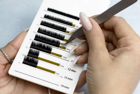 Beauty and fashion - eyelash extension procedure. Tweezers for eyelash extension in the hands of a...