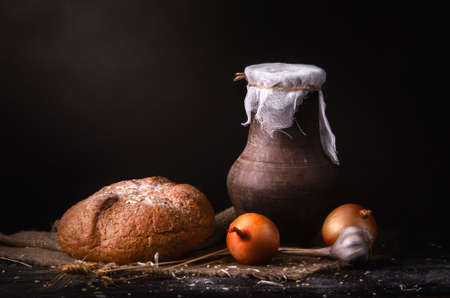 still life earthenware jug of milk on a table with drapery, bread, onions and chivesの写真素材