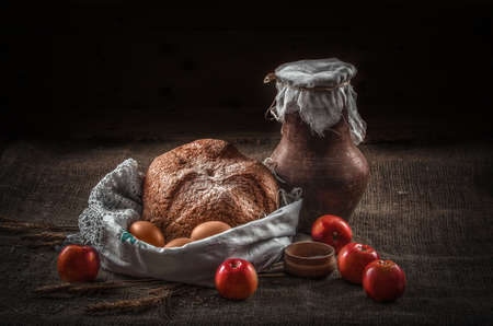 still life earthenware jug of milk on a table with drapery, bread, eggs and apples, rural foodの写真素材