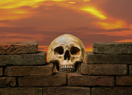 human skull behind the hole of old brick wall against twilight skyの写真素材
