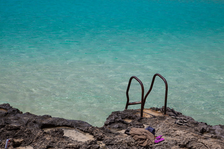 Rusty stairs on rocks to pool-like sea waters with flip-flopの写真素材