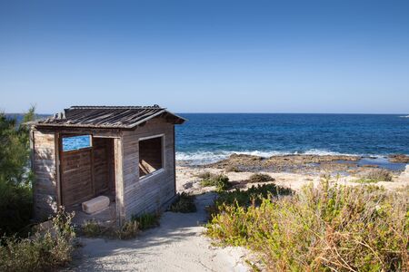 A service old wood house on a sunny beach with rocks and wavesの写真素材