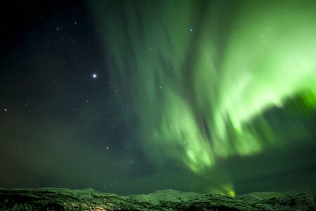 Strong bright green aurora northern lights over mountain, Tromso, Norway