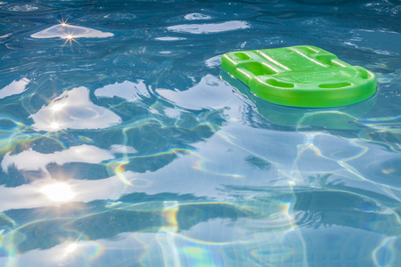 Green lifesaver floating in a swimming pool in summer time with sun reflectionの写真素材