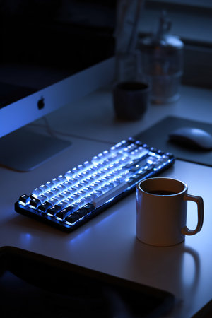 Modern workspace setup featuring a glowing RGB keyboard and a coffee mug.の素材
