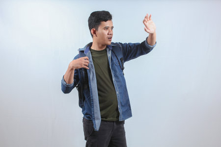 Asian man wearing denim shirt and backpack covering the sun with his handの写真素材