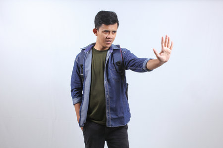 Asian man wearing denim shirt carrying school backpack thinking showing stop gesture isolated on...