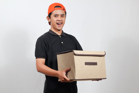 asian delivery man in black t-shirt and cap holding box on white background