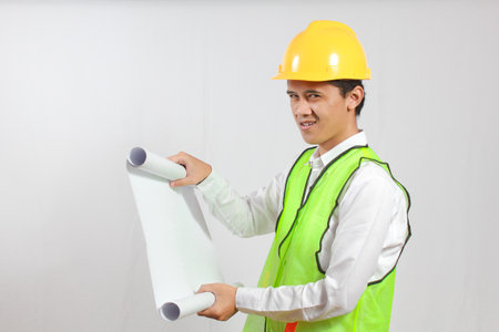 Portrait of a young Asian engineer holding blueprints on white background