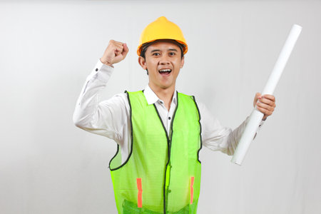 excited asian male engineer in hardhat with blueprints isolated on white background