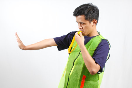 Young man wearing green overalls holding whistle on white background