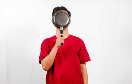 Young Asian man in red t-shirt holding frying pan on white background