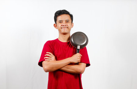 Portrait of a young Asian man holding a frying pan over white backgroundの写真素材