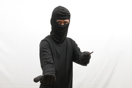 Thief in black mask and black hoodie pointing on white background