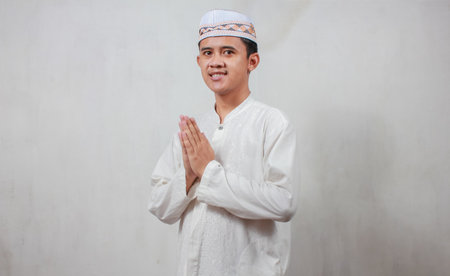 Portrait of young muslim man in traditional clothes praying over gray background